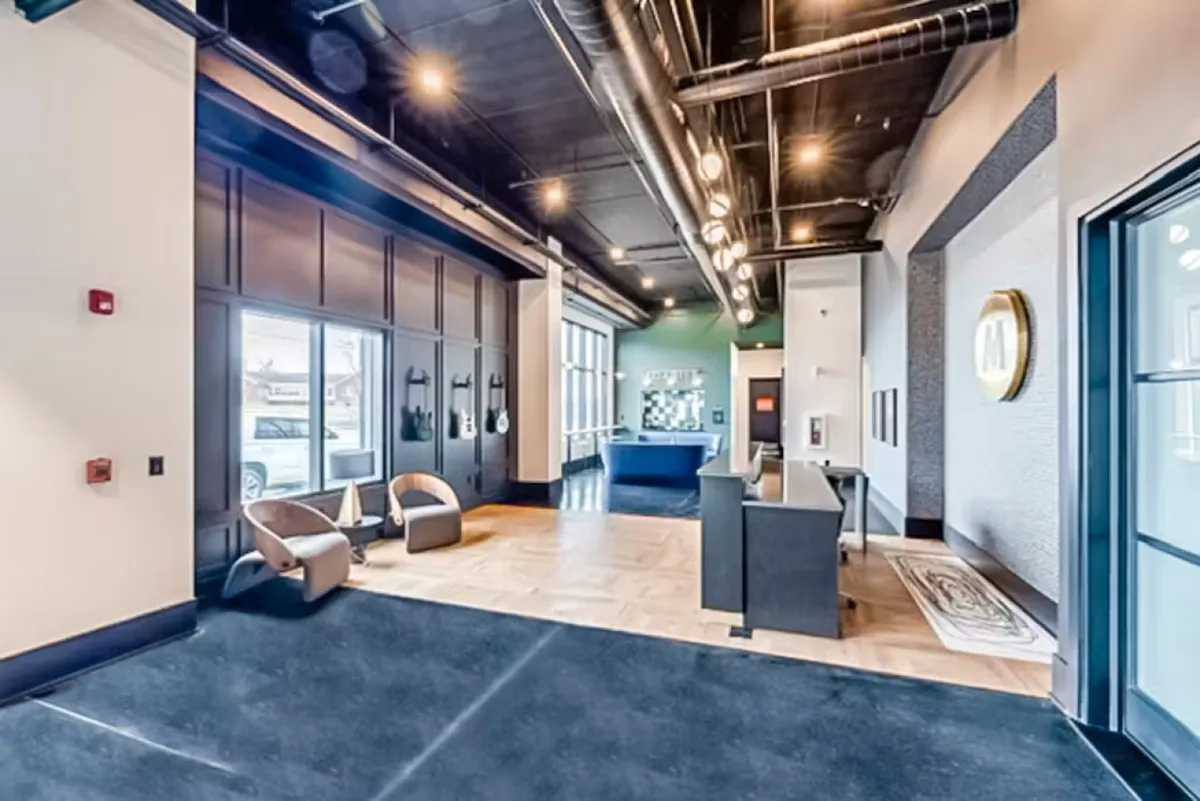 A modern seating area with contemporary chairs, a stylish reception desk, wall art, and large windows letting in abundant natural light. The ambiance is inviting and suggests a hotel-like guest experience, echoing the section's promise of hotel-style amenities in a private residence.
