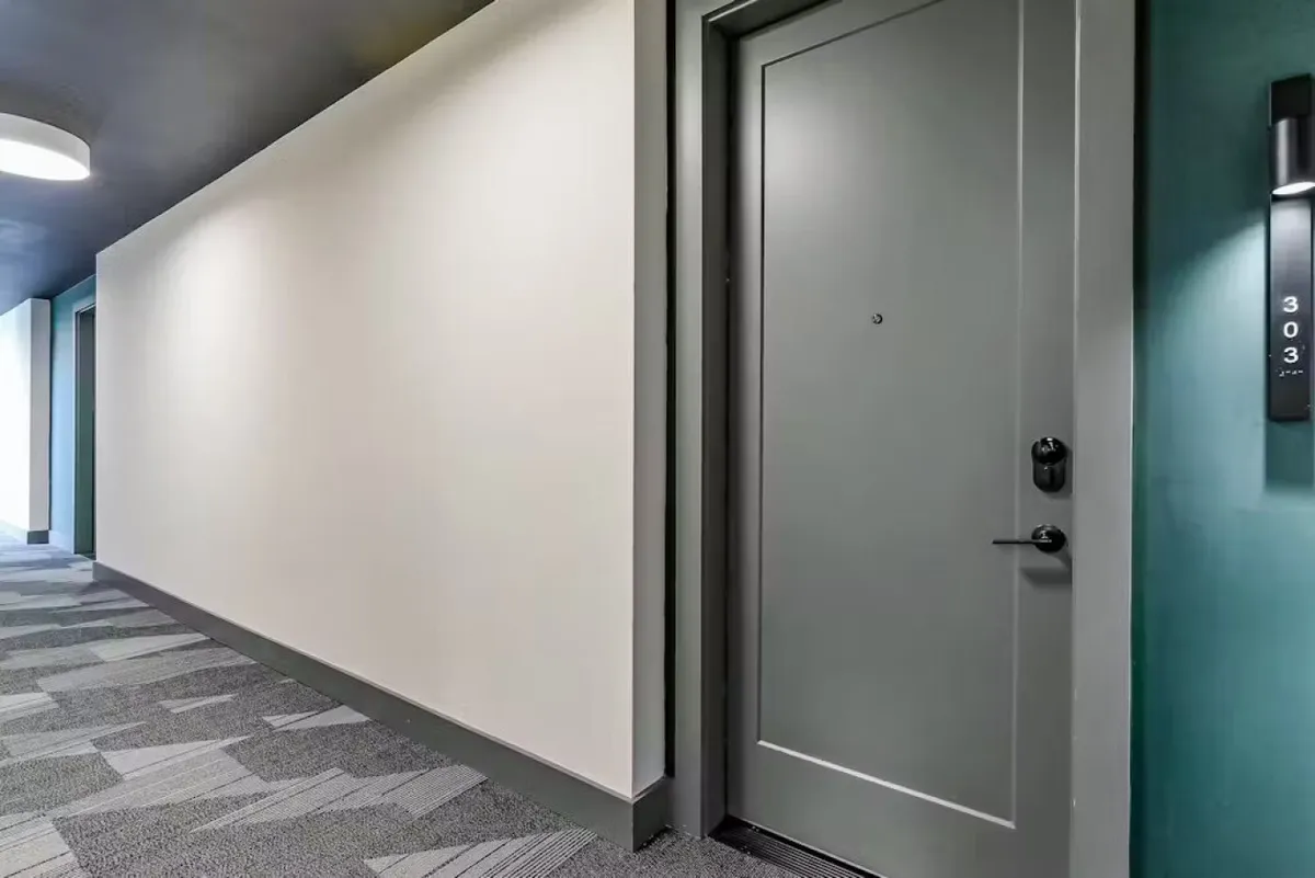 This image captures the entryway to Room 303, featuring a welcoming doorway, soft hallway lighting, and a textured carpet. The scene conveys a sense of arrival and first impressions, aligning directly with the section's emphasis on seamless entry and the start of the guest experience.