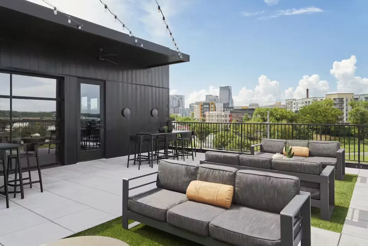 This image shows a stylish outdoor seating area overlooking the Nashville city skyline. String lights create a warm ambiance, and lush green plants bring a touch of nature. The seating is arranged for socializing and relaxation, perfect for enjoying the city's energy from the comfort of your own home base.