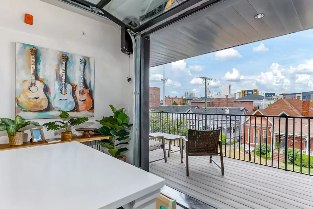 A bright, creative indoor scene featuring a wall with guitar artwork, lush indoor plants, and a glimpse of an outdoor seating area. The space suggests a connection between indoor relaxation and outdoor enjoyment, with a nod to Nashville’s musical spirit.