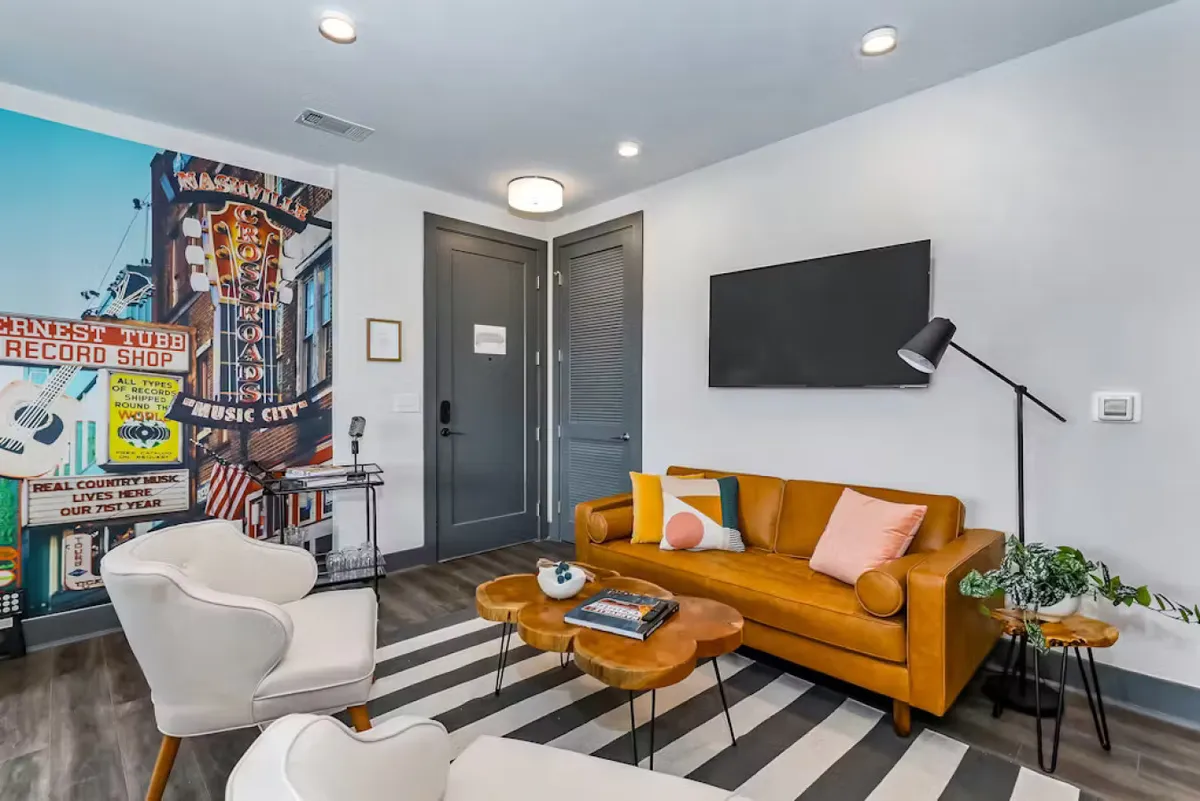 A cheerful living space featuring an orange couch, a bold striped rug, a vibrant wall mural, and a coffee table. The room radiates energy and comfort, highlighting a fresh, professionally cleaned environment ideal for relaxing and making memories.