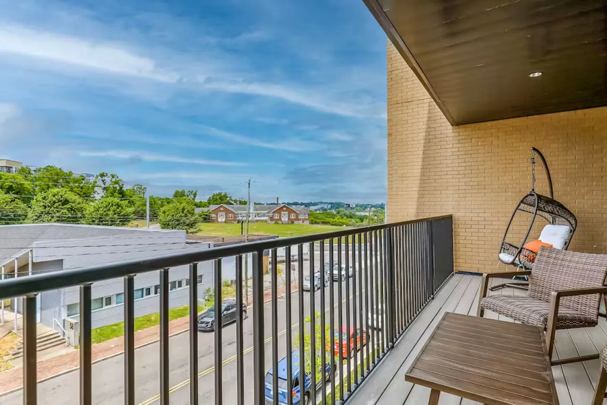 An inviting private balcony with a hanging chair, outdoor seating, and views of the street and greenery. The space is designed for relaxing outdoors, enjoying morning coffee, or socializing during sunset, bringing the outdoors in.