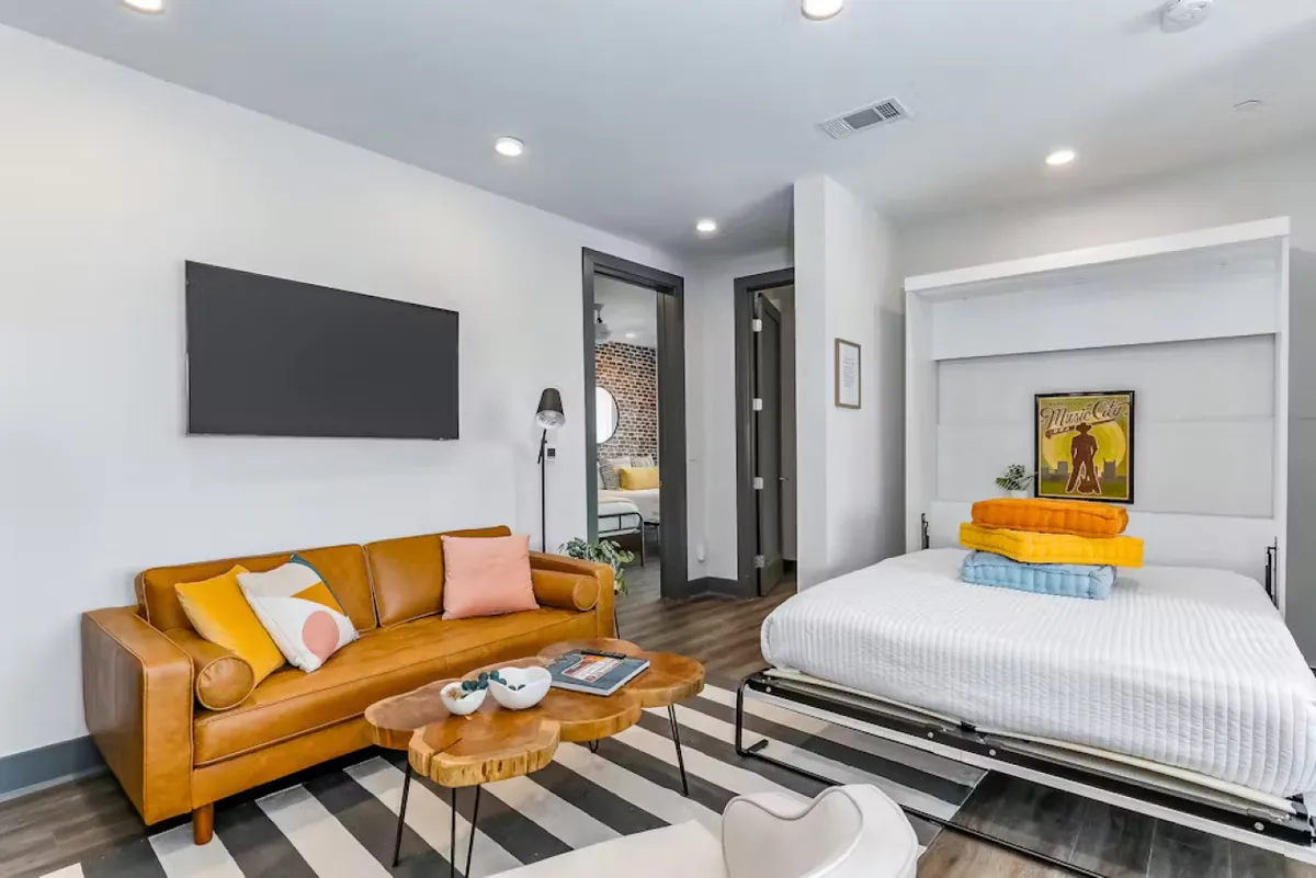 This image features a comfortable living room setup with a sofa, folding bed (Murphy bed), coffee table, television, and artwork adorning the walls. The arrangement invites social gatherings, relaxation, and casual entertainment, echoing the open-concept social space described in the section.