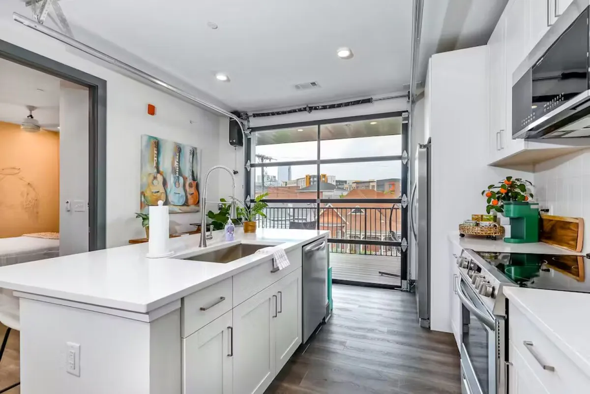 A bright, casual kitchen scene anchored by a large kitchen island, with guitars on the wall and expansive windows. The layout suggests an inviting space for both food preparation and creative gatherings, complemented by warm natural light.
